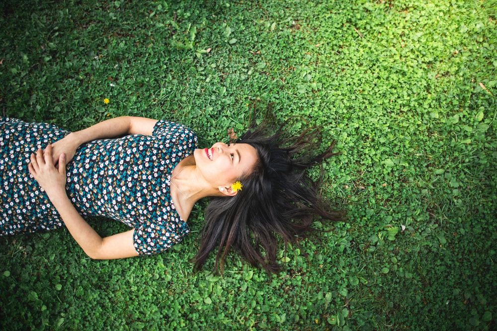 Nainen makaa ruohikossa rentoutuneena ja hymyilee