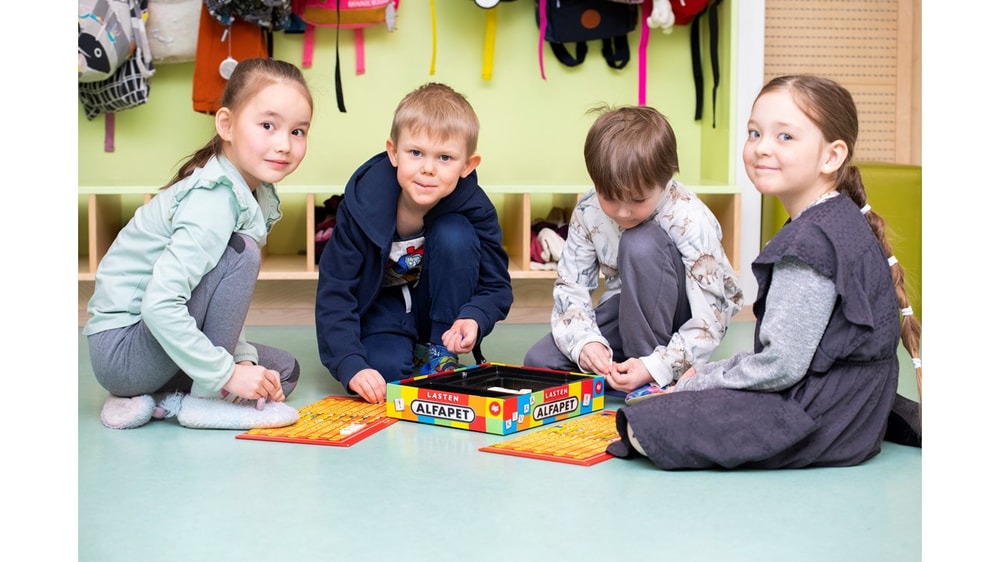 Lapsia istumassa vierekkäin lattialla lautapelin äärellä