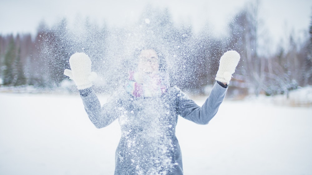 Tyttö heittää lunta ilmaan talvimaisemassa