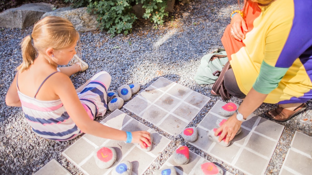 Lapsi ja aikuinen pelaa risti nollaa kivillä tehdyillä pelimerkeillä.
