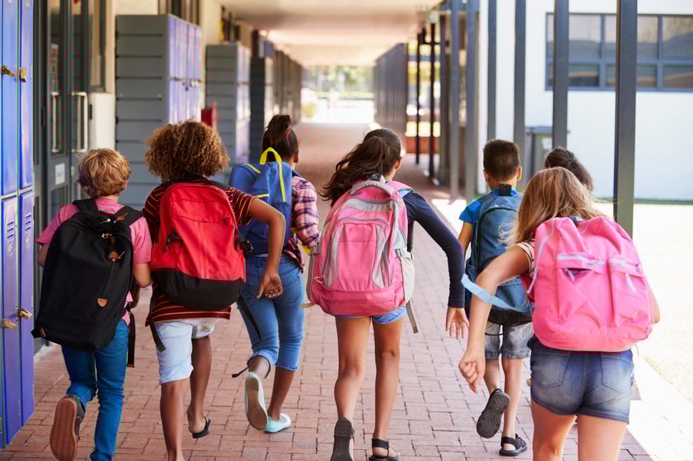 Lapset juoksevat koulun pihassa reput selässään poispäin kuvaajasta