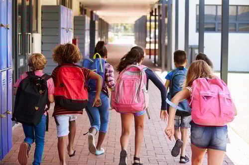 Lapset juoksevat koulun pihassa reput selässään poispäin kuvaajasta
