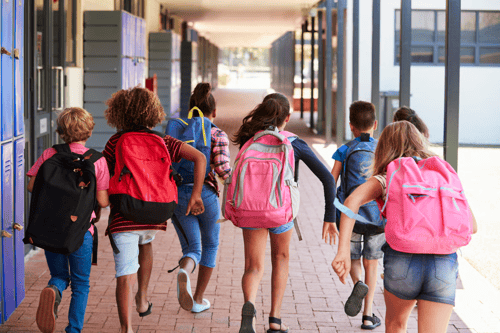 Lapset juoksevat koulun pihassa reput selässään poispäin kuvaajasta